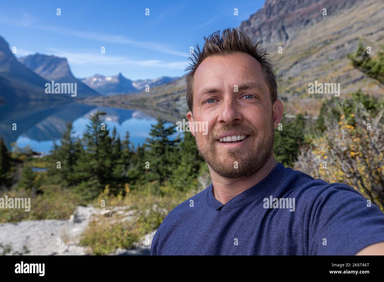 Young man taking a selfie at the St Mary viewpoint in glacier National Park with beautiful calm conditions Stock Photo
