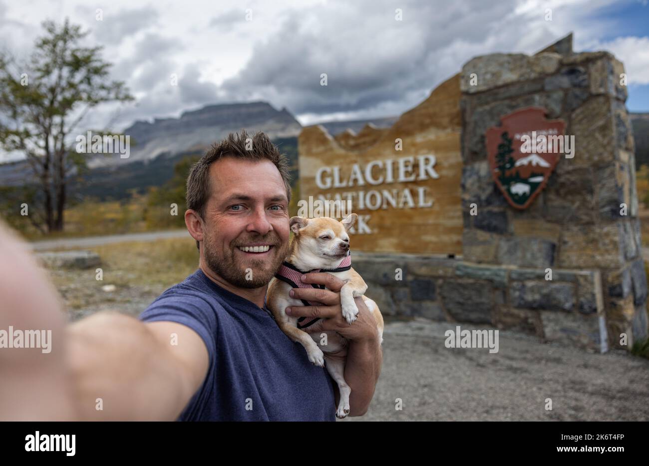 Man and his best friend a chihuahua taking a selfie in front of the welcome sign for Glacier National Park in Montana Stock Photo