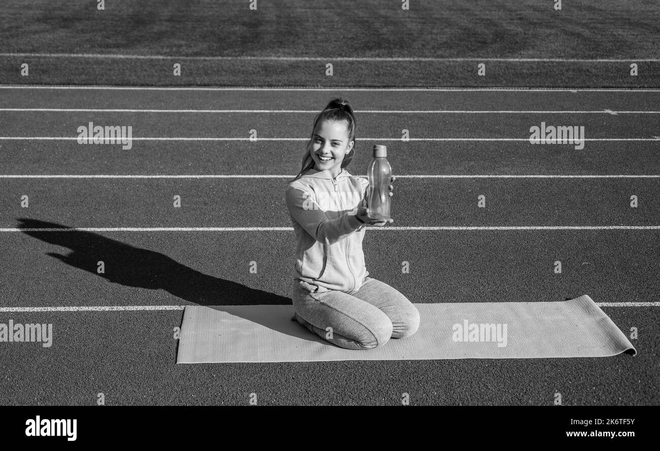 Drink water during fitness workout. Happy child show bottle sitting on