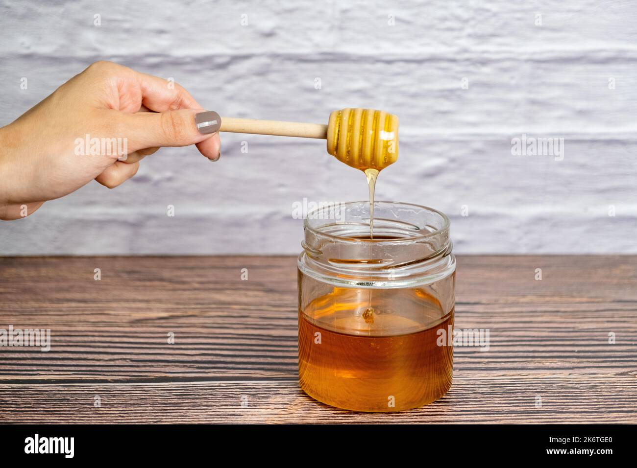 Honey drizzling. Pot of honey and wooden stick isolated white brick ...