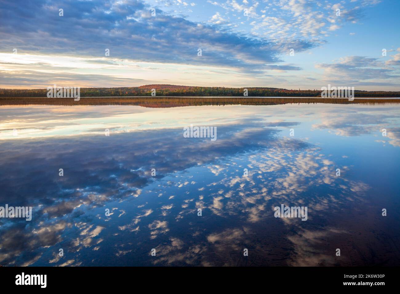 Beautiful calm lake with cloudscape reflecting and hills with trees in autumn color in northern Minnesota Stock Photo