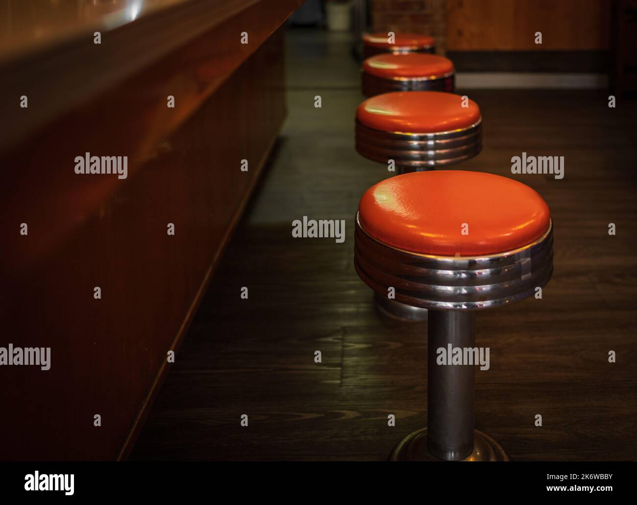 Vintage stools in the restaurant. Row vintage stools in front of wooden counter inside a vintage style bar. A row of four shiny red vinyl stools. Nobo Stock Photo
