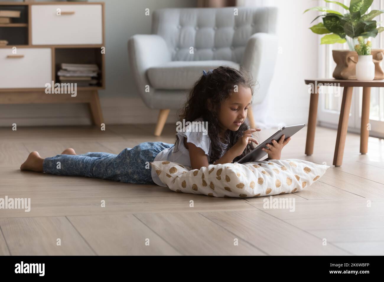 Little Indian girl lying on warm floor using digital tablet Stock Photo ...