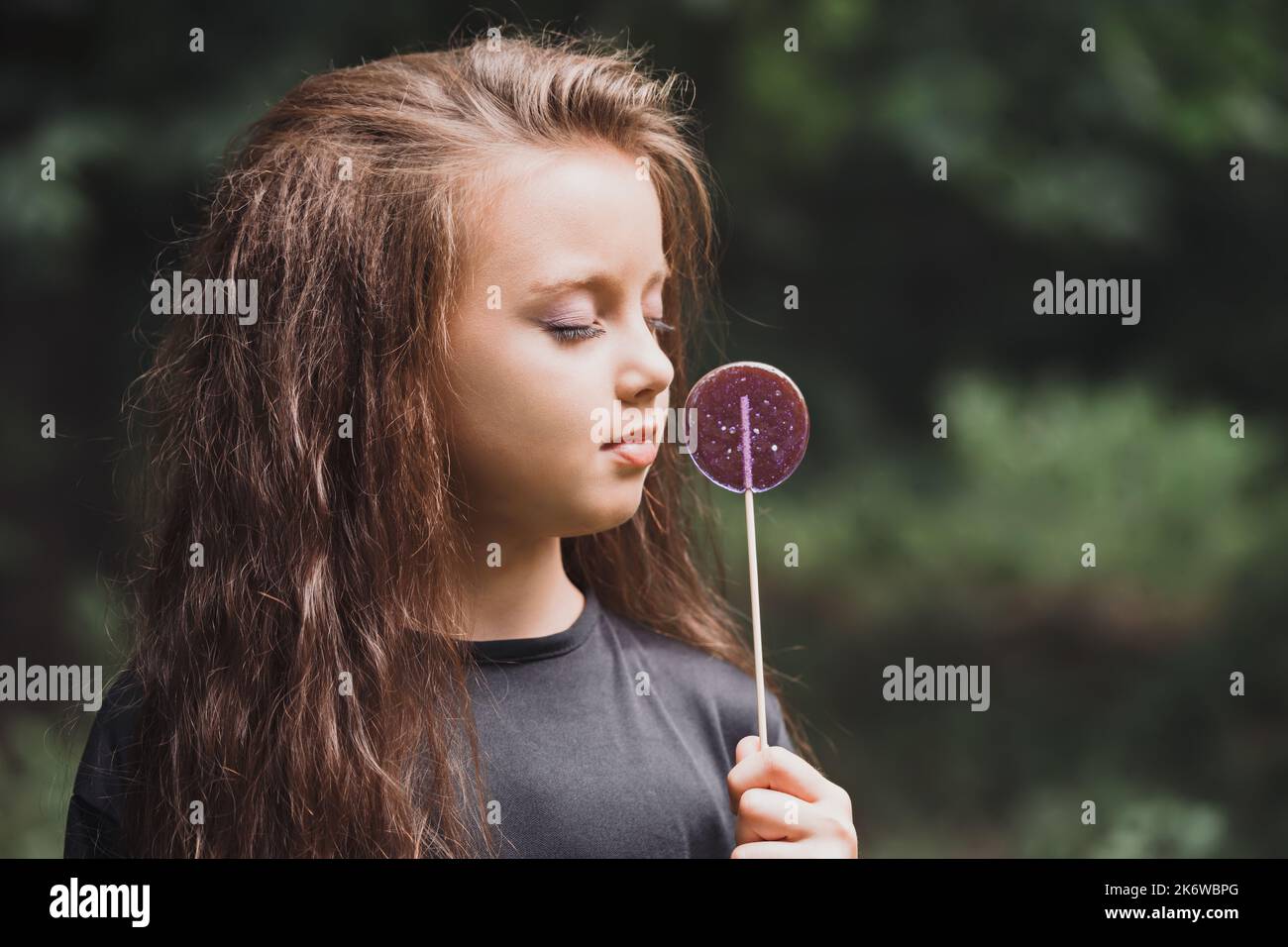 A cute girl in black clothes with a purple candy on a stick Stock Photo