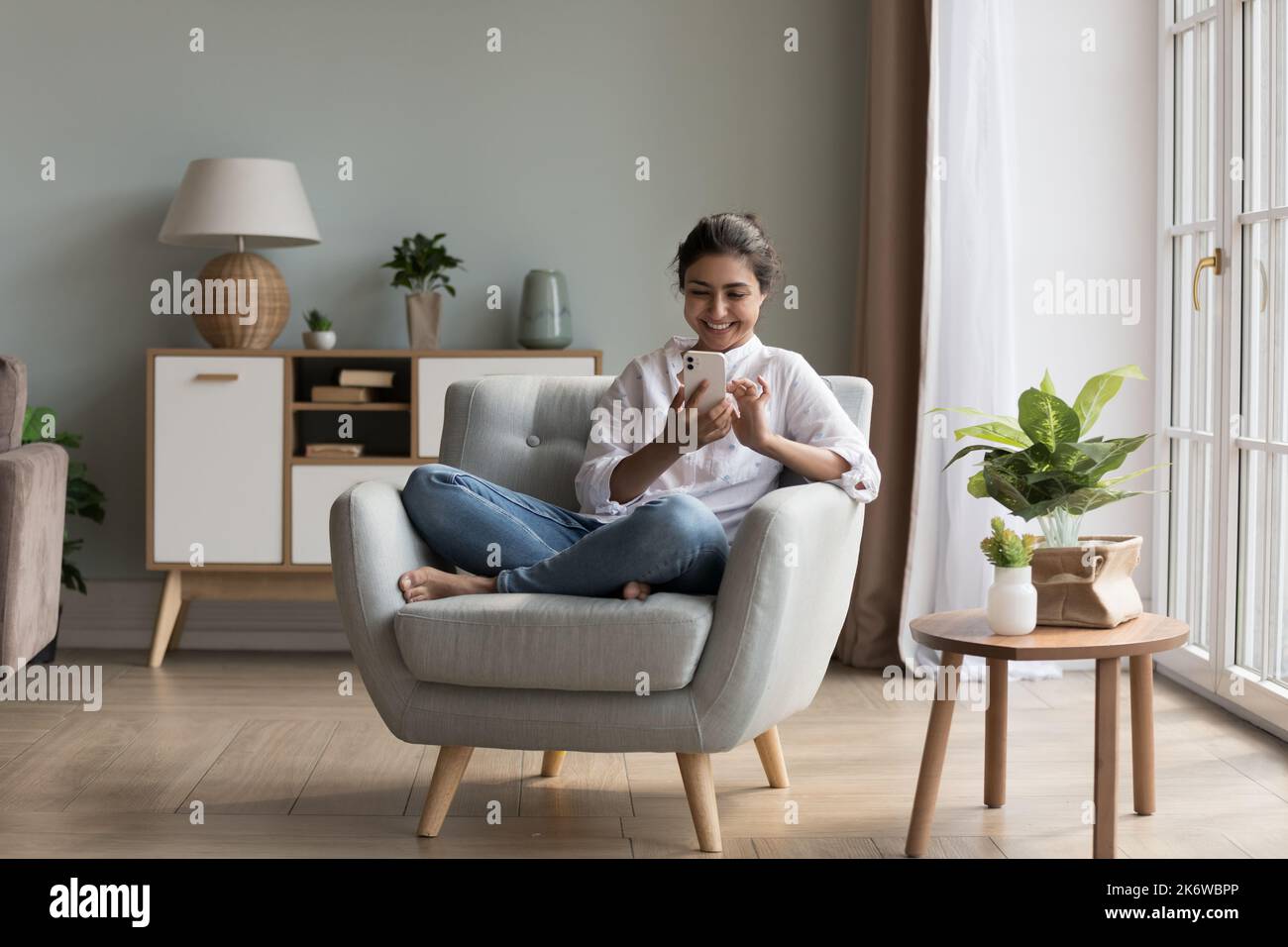 Beautiful Indian woman use smartphone relaxing on armchair Stock Photo ...