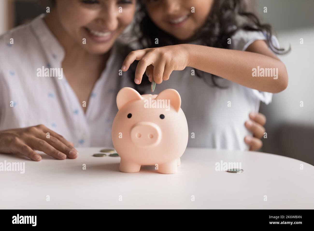 Smiling Indian mom and little daughter dropping coins into piggybank Stock Photo