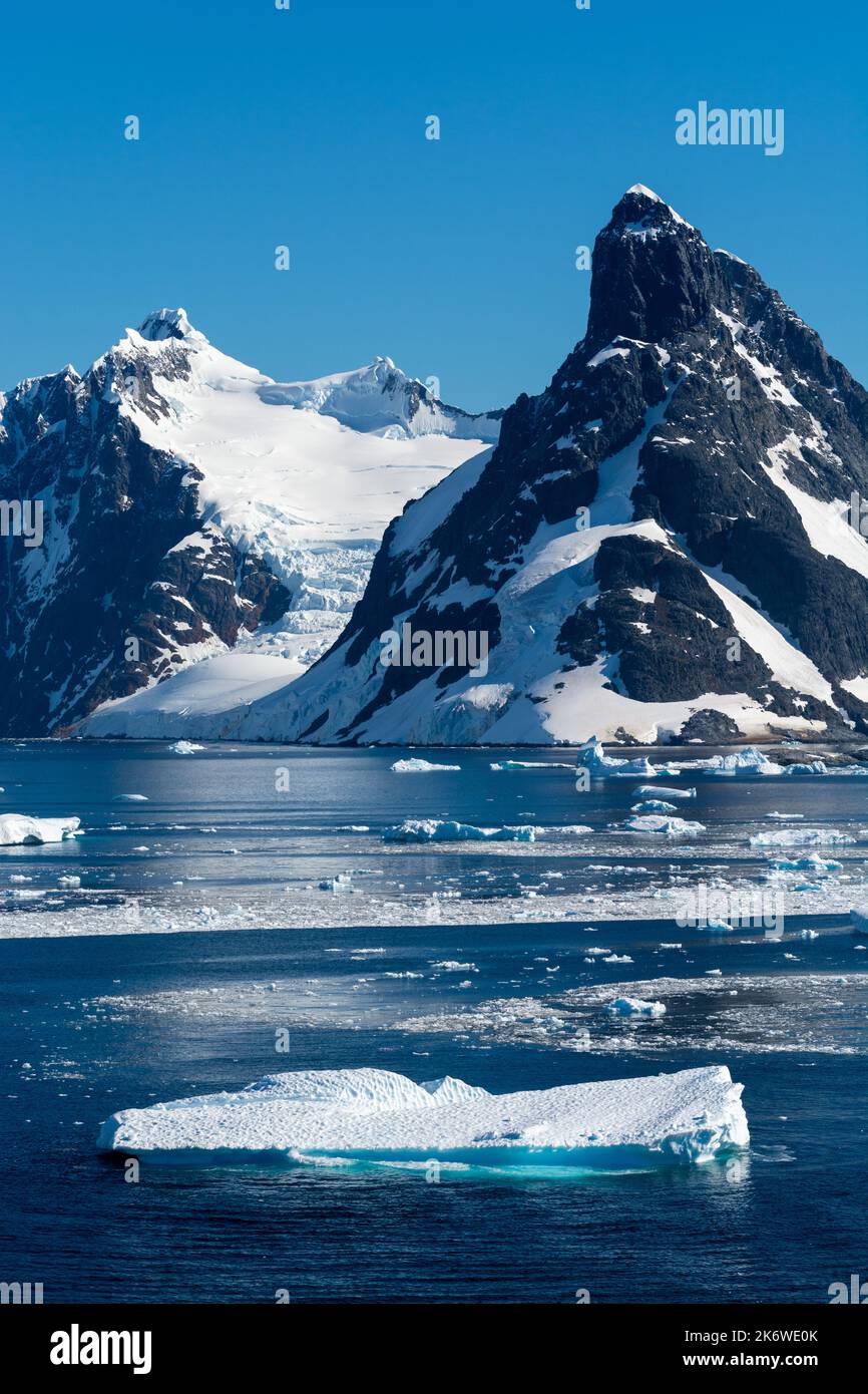 brash ice and icebergs floating on waters of northern approach to lemaire channel (kodak gap, kodak alley) with booth island and mt. lacroix (r). wilh Stock Photo
