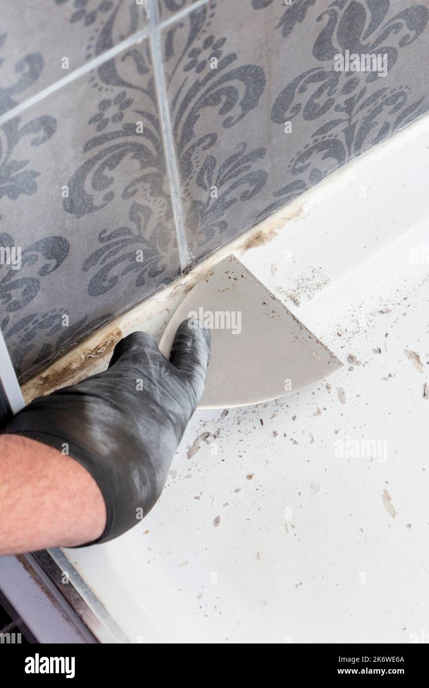 Man scraping silicone sealant from around the base of a shower cubicle
