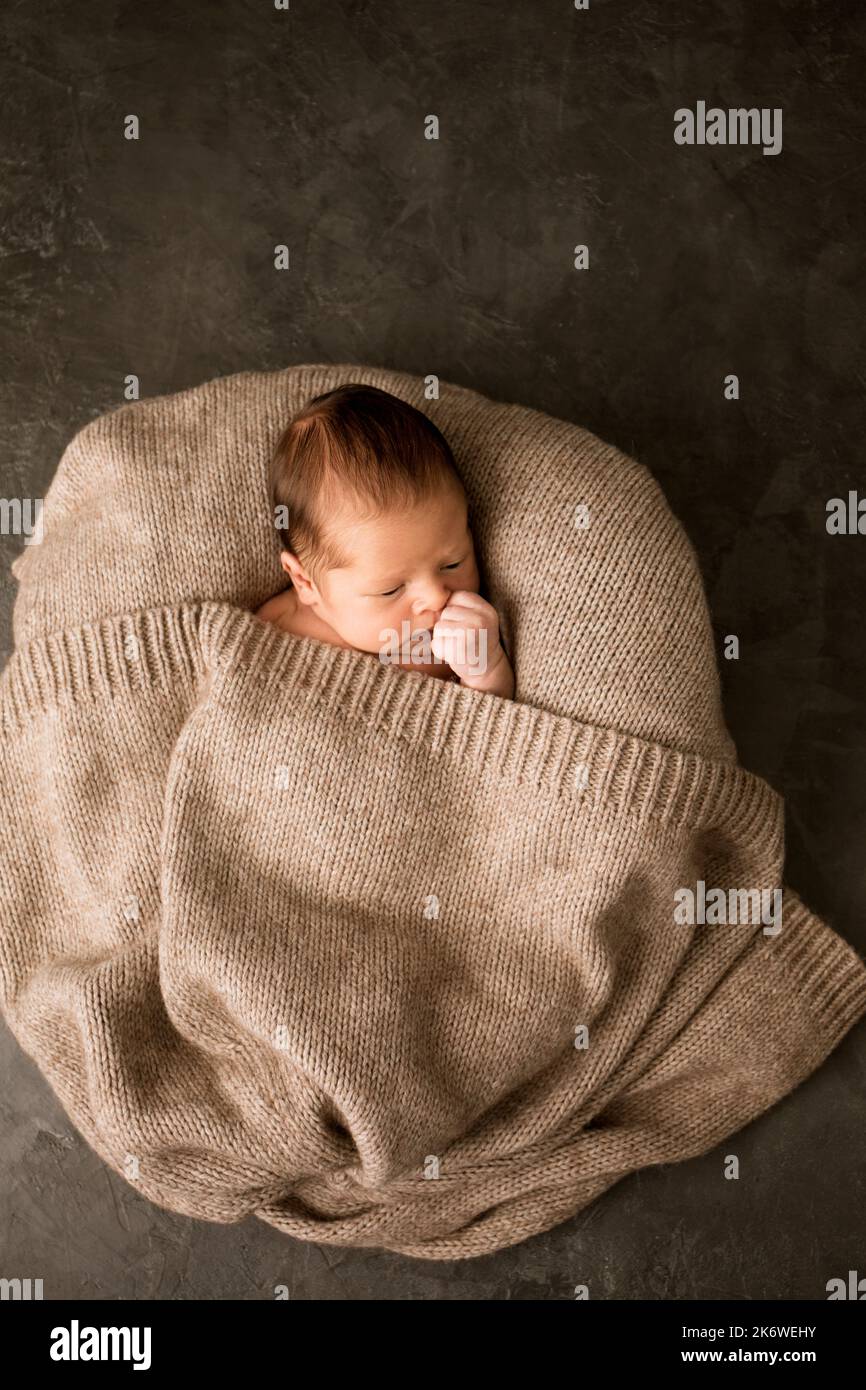 A newborn baby covered with a warm knitted blanket on a dark background Stock Photo