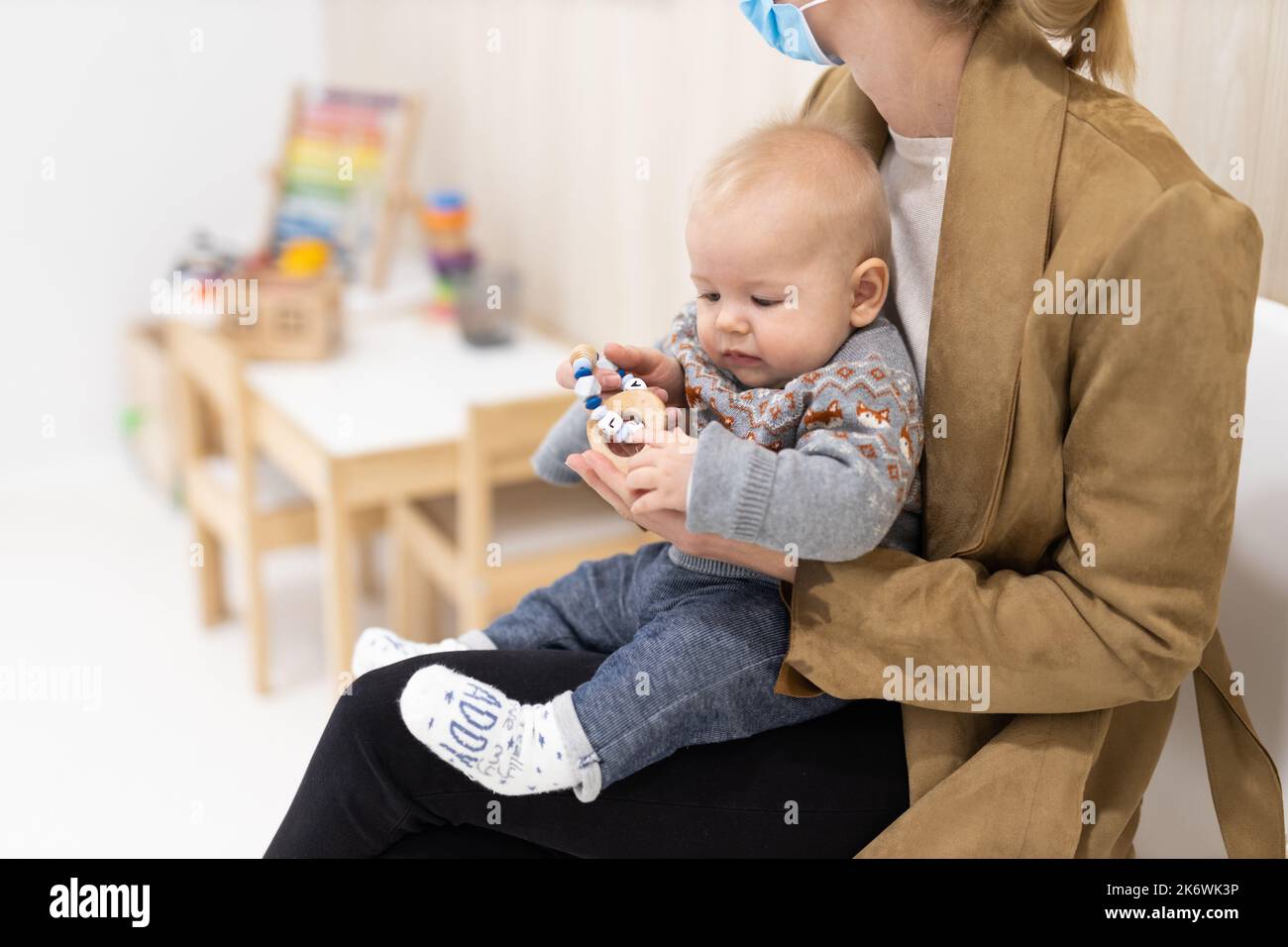 Mother holding infant baby boy in her lap, sitting and waiting in front of doctor's office for pediatric well check. child's health care concept Stock Photo