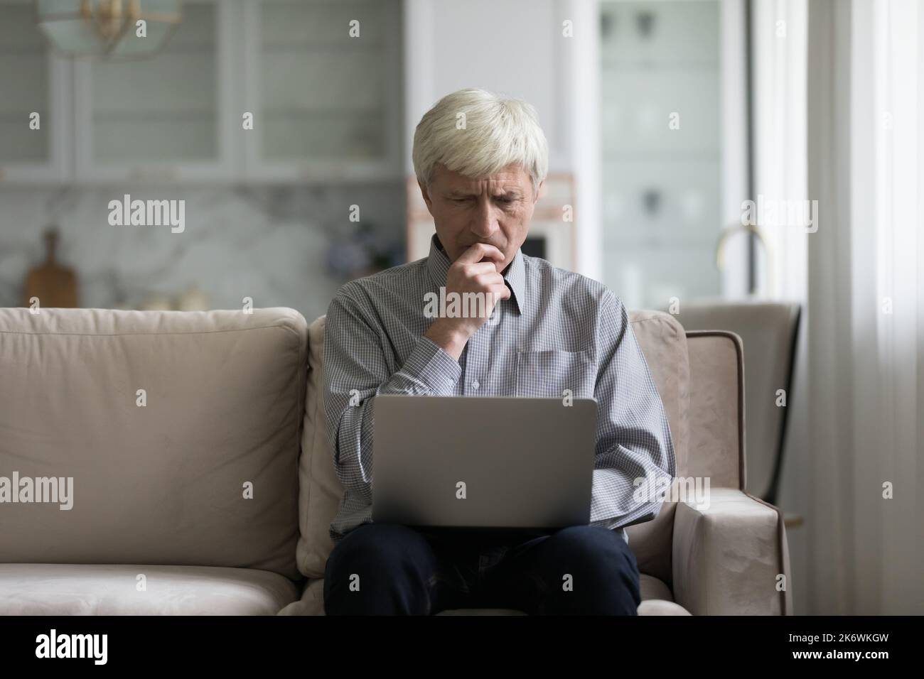 Frown older man sit on sofa with laptop Stock Photo