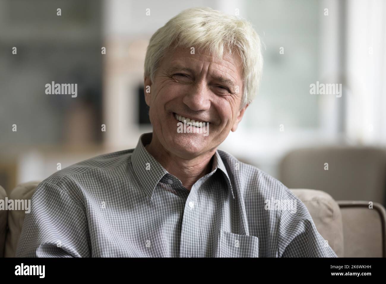 Smiling aged man sit on sofa staring at camera Stock Photo