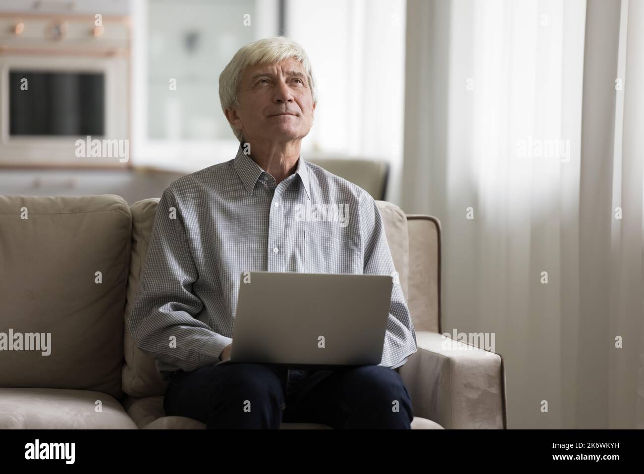 Pensive senior man sits on sofa with laptop Stock Photo