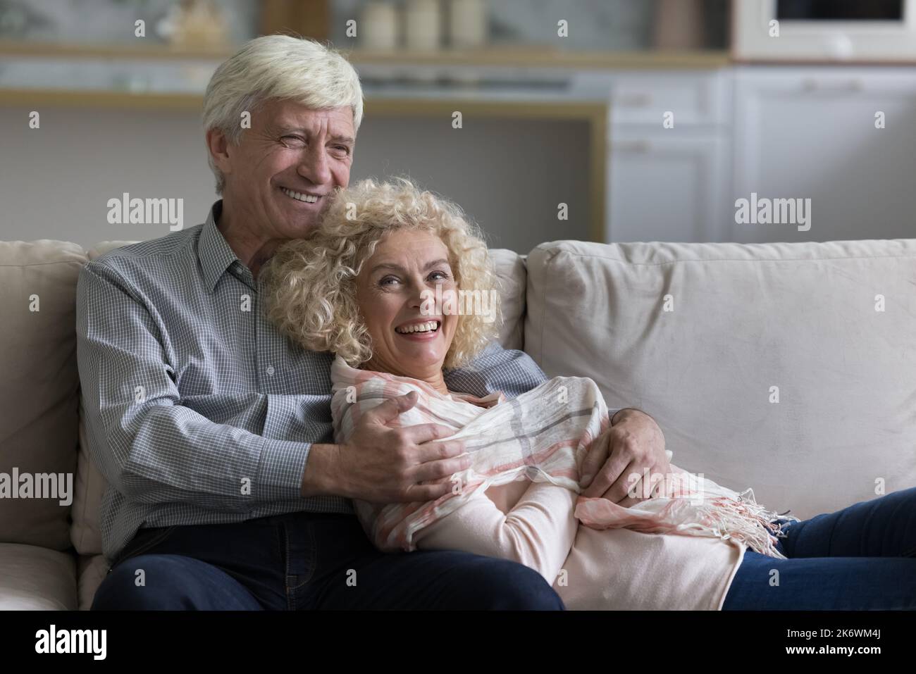 Attractive loving older spouses resting together on comfortable sofa Stock Photo