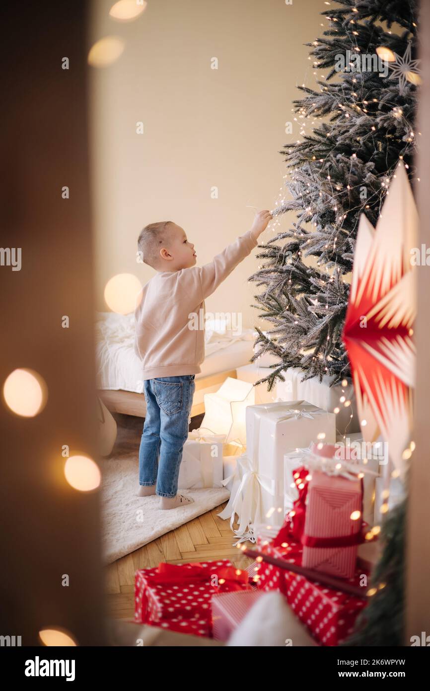 Cute little boy at home during winter holiday. Boy decorated Christmas tree and lot of presents Stock Photo