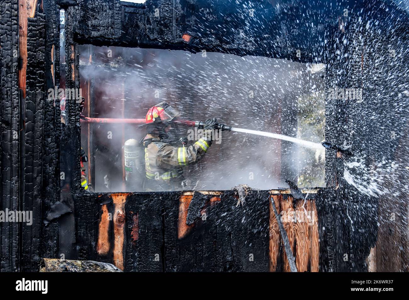 A firefighter uses a hose to extinguish hot spots and soak down the walls as members of the Springs Fire Department, along with mutual aid from member Stock Photo