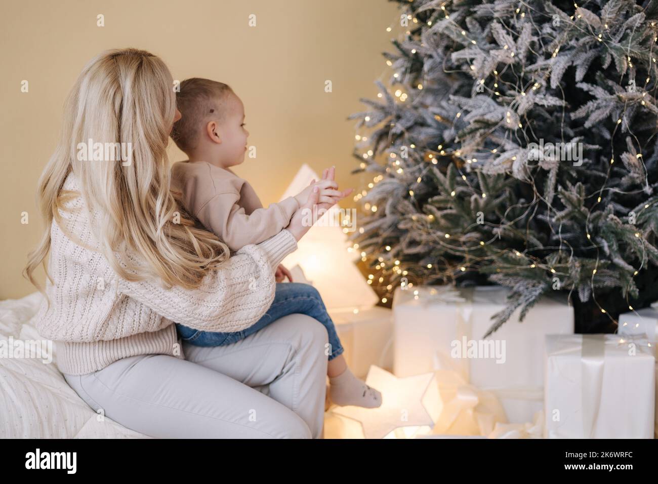 Portrait of mom with her little son decorated Christmas tree at home. Cute boy help his mother preparing for holidays Stock Photo