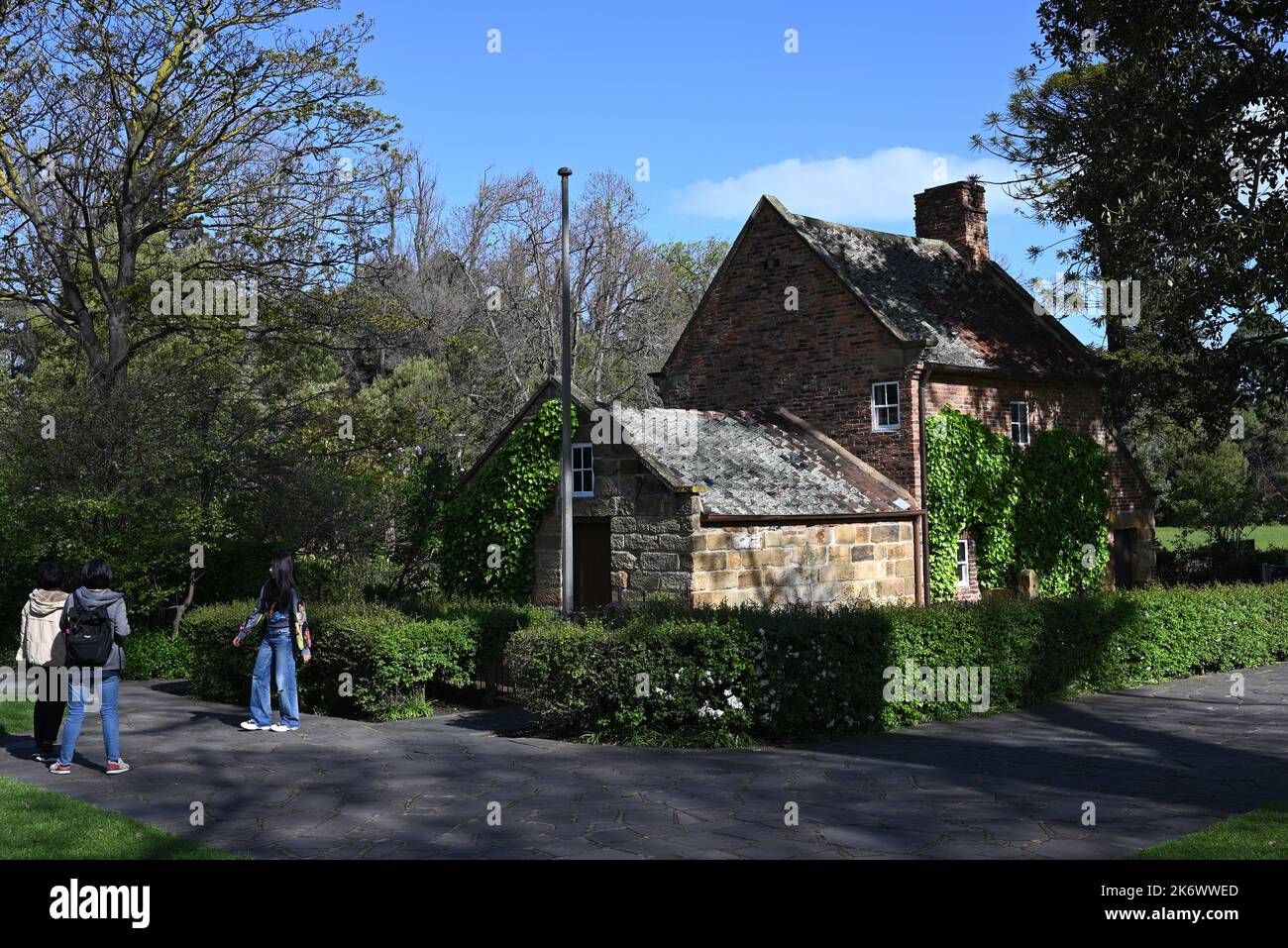 Cook's Cottage amongst the trees of Fitzroy Gardens, as a visitor poses for a photograph in front of the historical landmark Stock Photo