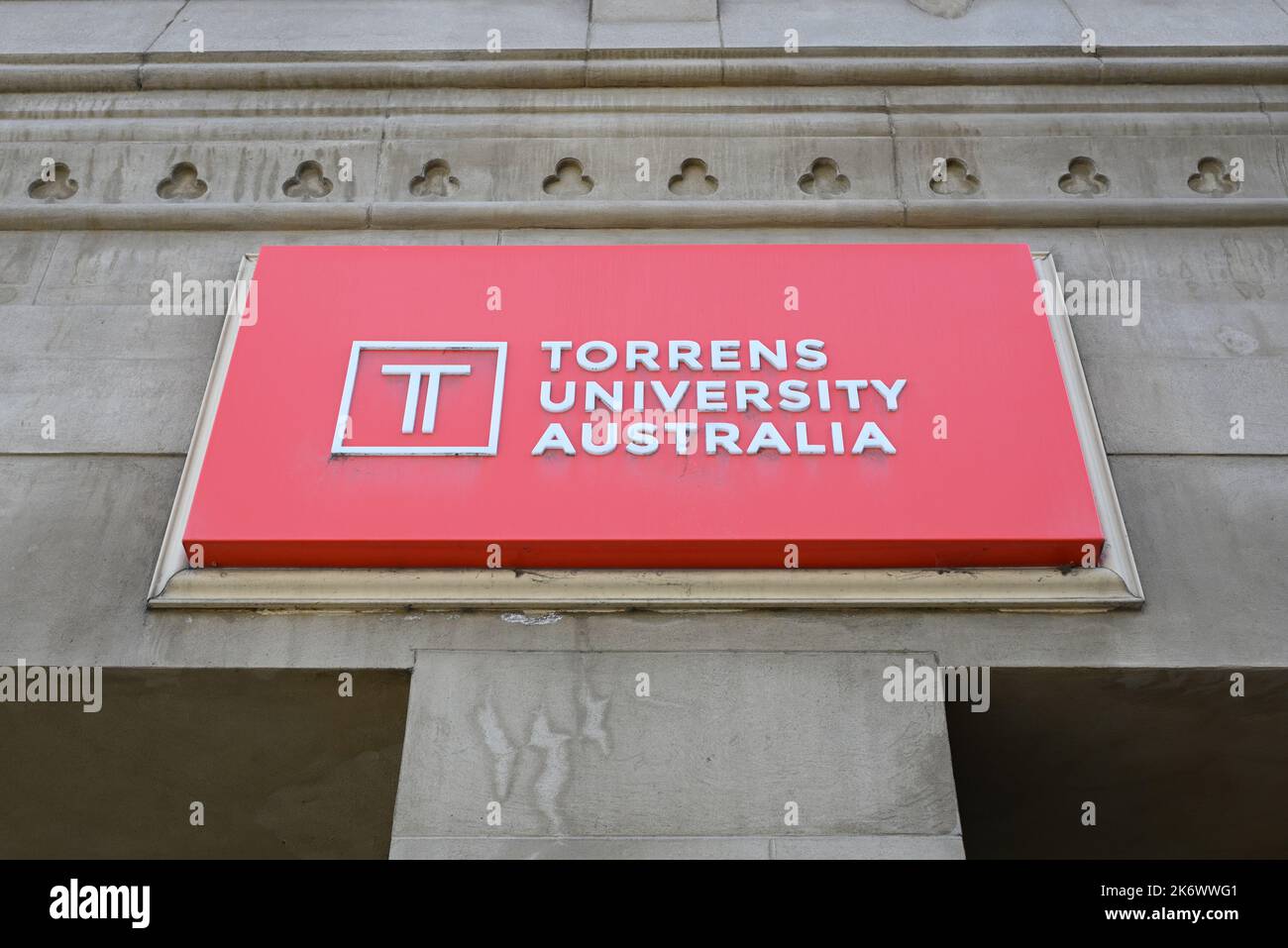Red and white Torrens University sign, above the entrance to its Flinders St campus, with logo and lettering covered in cobwebs Stock Photo