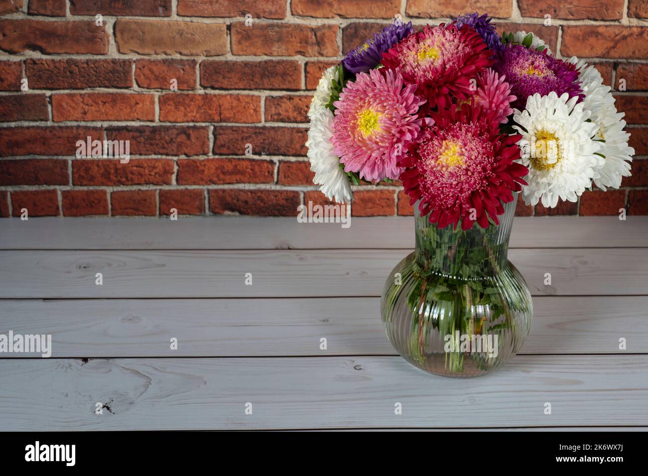 Beautiful bouquet of asters on white wooden table in front of brick wall Stock Photo