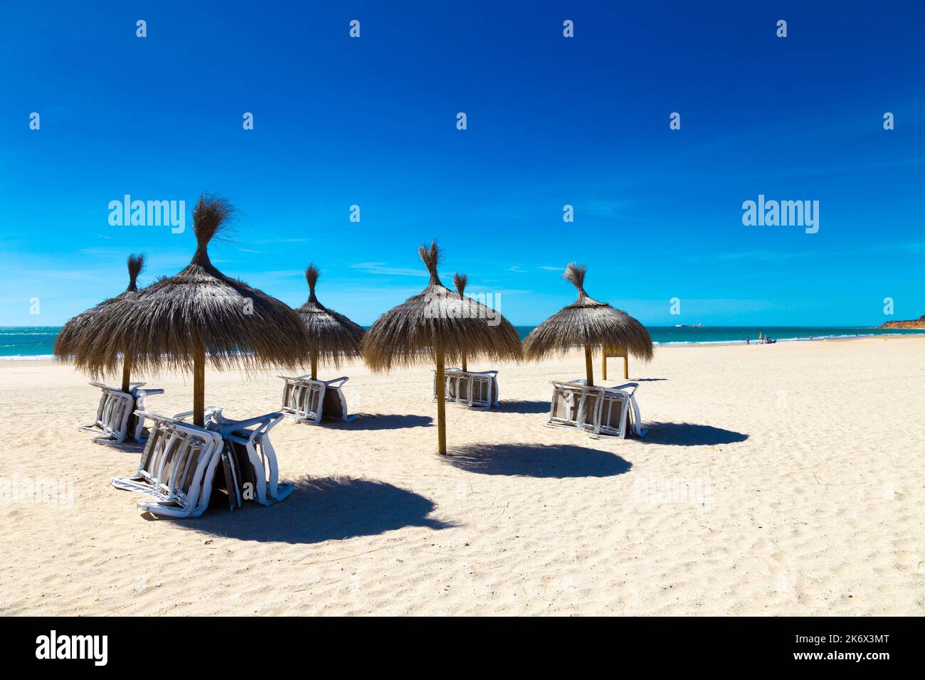 Straw parasols, white sand and blue sky at Playa de la Barrosa, Costa de la Luz, Cadiz, Spain Stock Photo