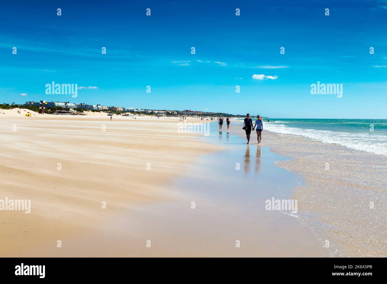 Dry sand swept by wind across the beach, people walking along Playa de la Barrosa, Cadiz, Spain Stock Photo