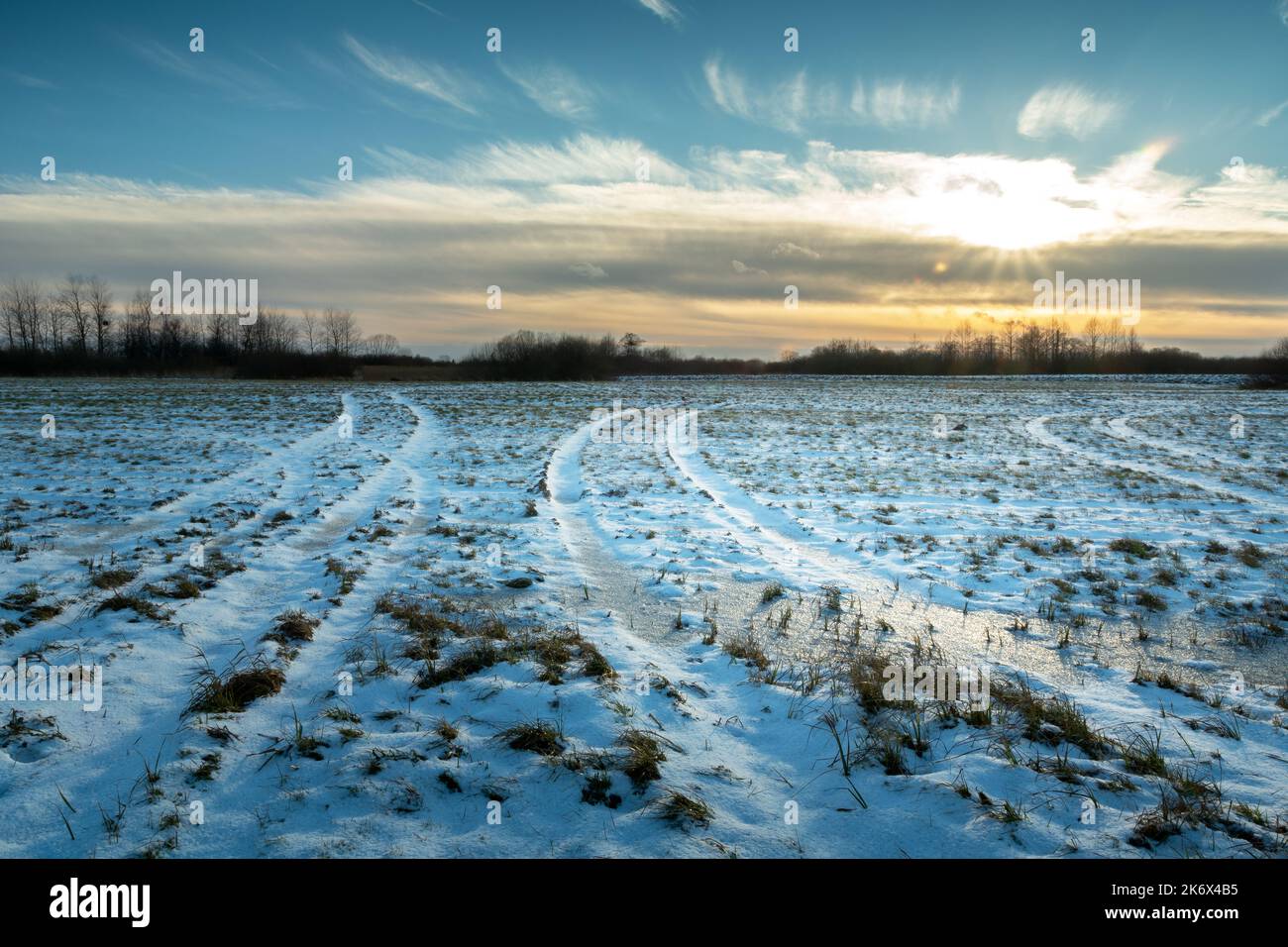 Winter landscape with a farmland and the setting sun behind the clouds Stock Photo