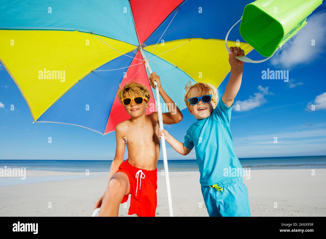 Two cute kids in sunglasses under parasol on a sand ocean beach Stock