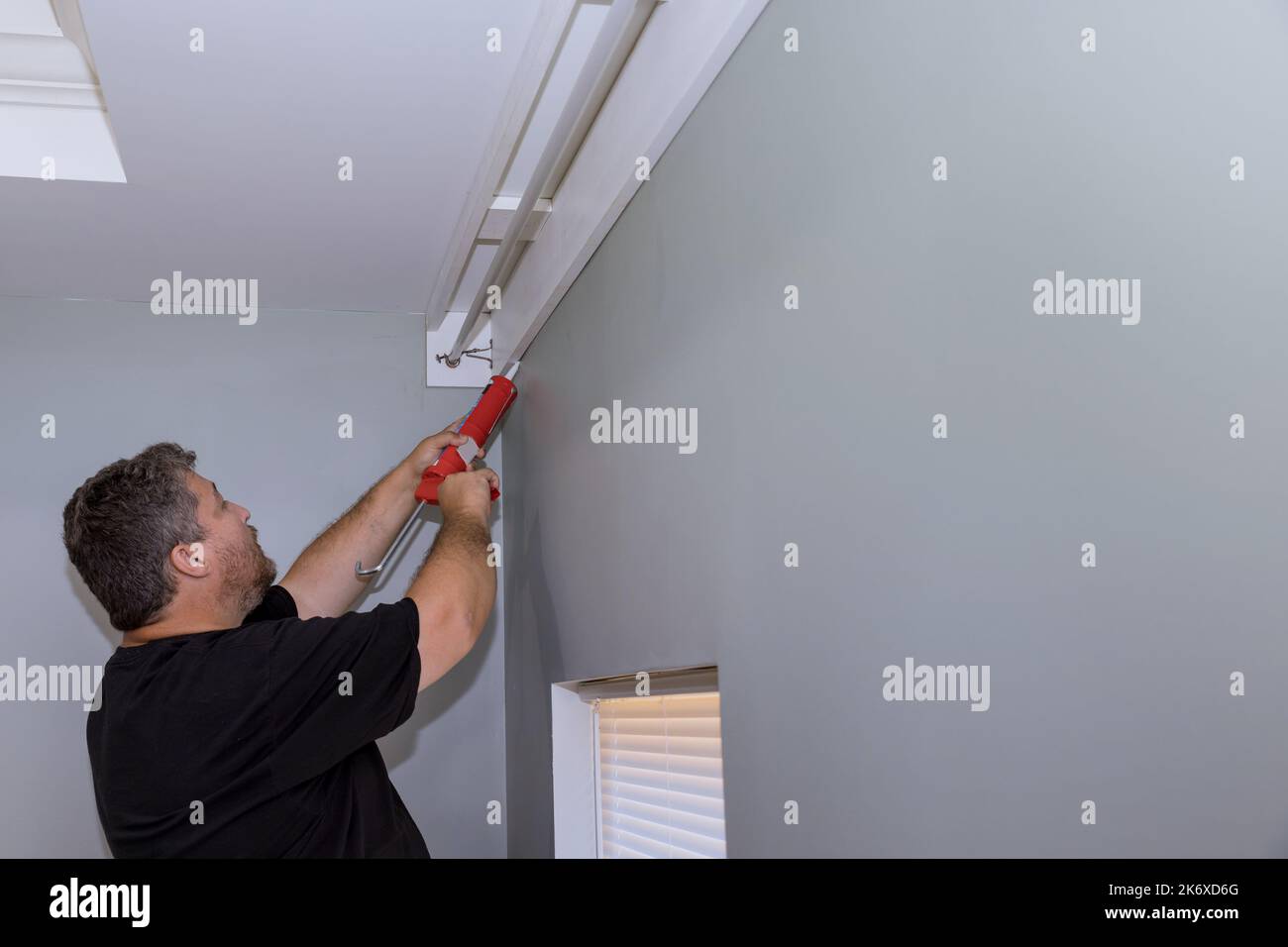Construction worker syringe fills seam between cornice and wall with