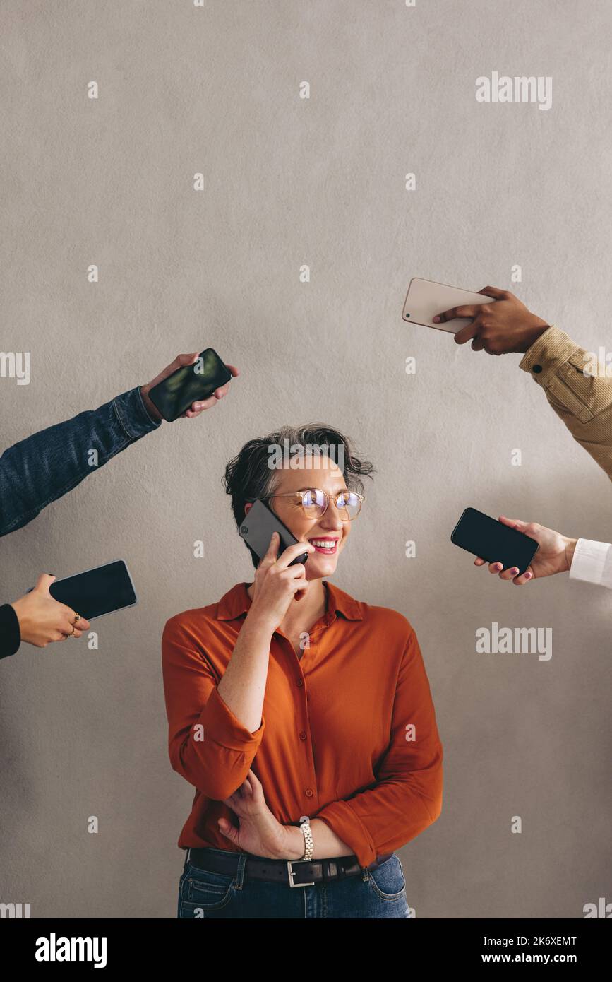 Happy businesswoman speaking on the phone while surrounded by hands holding smartphones. Cheerful businesswoman smiling while answering phone calls in Stock Photo