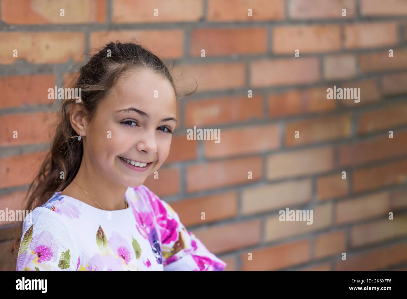 Portrait of pretty little girl smiling at the camera. Brick wall is in ...