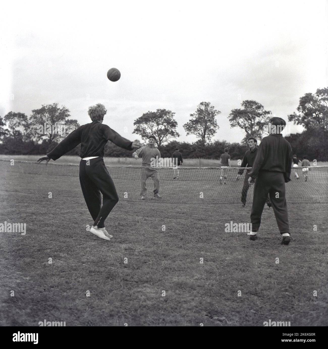 1960s, historical, footballers of Aylesbury United FC in the cotton tracksuits of the era, out on a large grass fieid, doing some pre-season training by keeping a football above a net, Aylesbury, Buckinghamshire, England, UK. Stock Photo