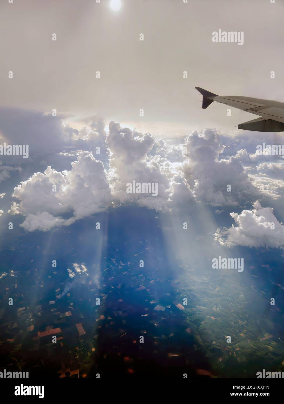 Aerial view flying above dramatic fluffy clouds and sun rays piercing shining through the clouds, sunny cloudscape, sunlight, part of airplane, wing, Stock Photo