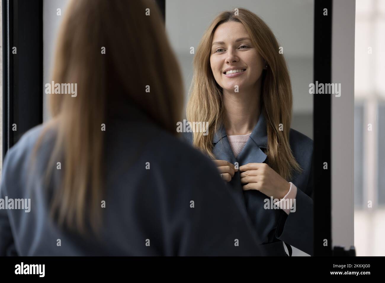 Woman wears dark casual coat standing indoors looks in mirror Stock Photo