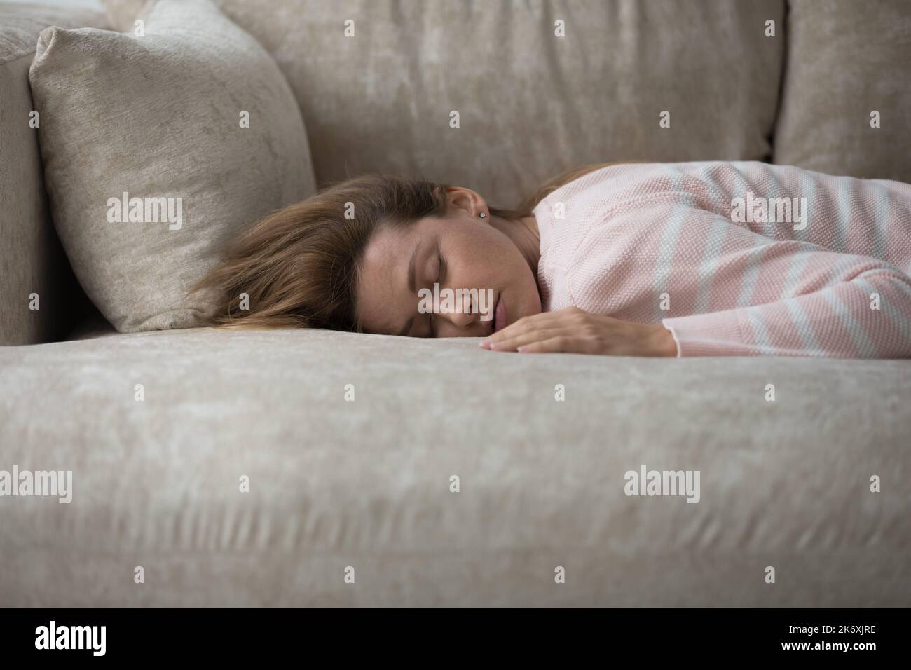 Tired woman has nap lying on sofa looks without energy Stock Photo