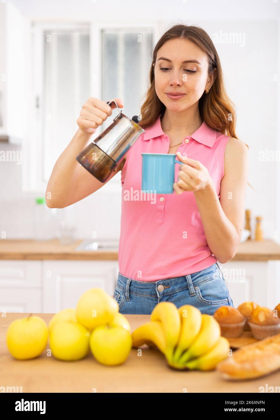 Smiling brown-haired woman enjoying cup of coffee in home kitchen Stock Photo