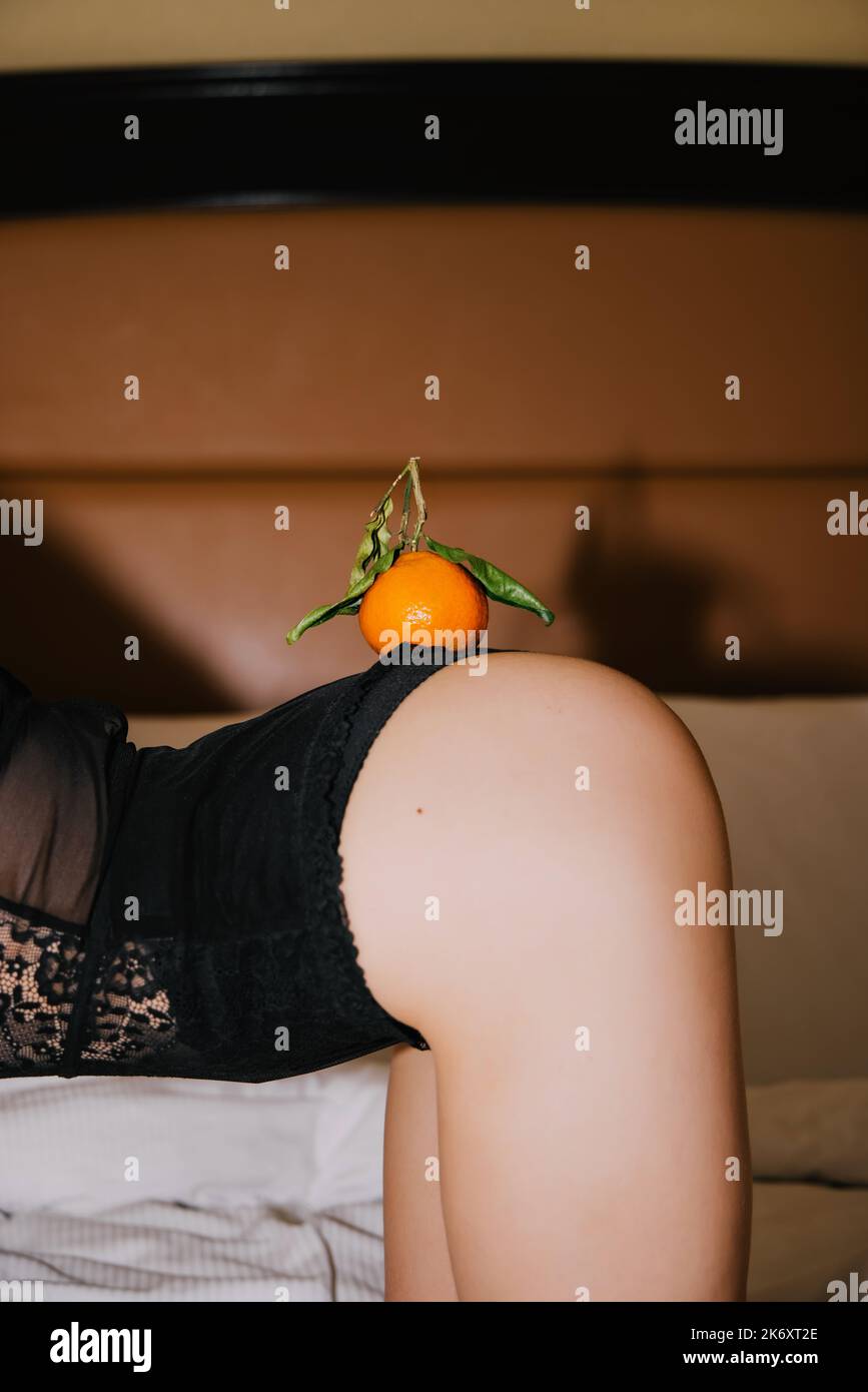 Closeup of orange tangerine with green leaves on the back of a girl wearing black lingerie on a bed; no face visible Stock Photo