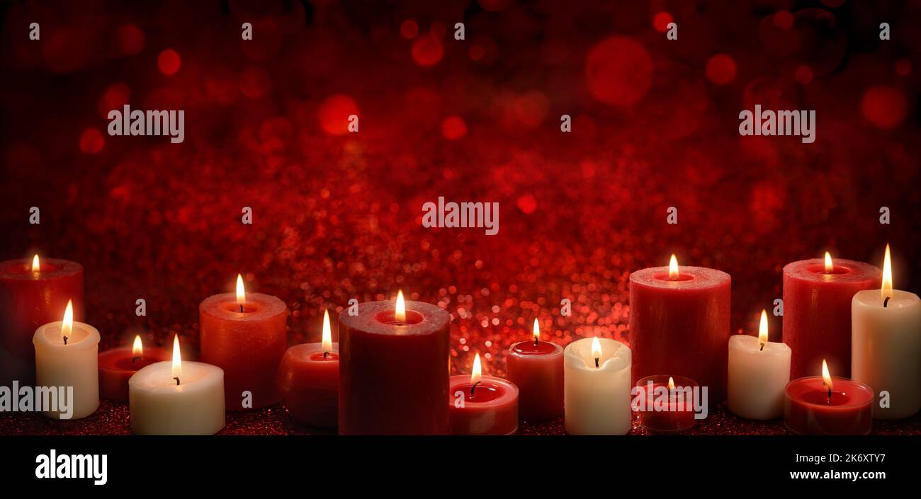 Burning candles as a border on a red festive background with glittering bokeh lights, ideal for Christmas or religious events, wide format with copy-s Stock Photo