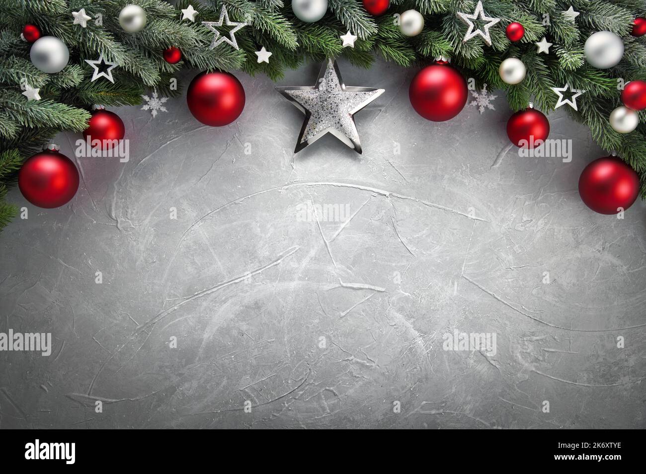 Elegant modern Christmas background with an arch-shaped border composed of fir branches, red and silver baubles and stars, on gray textured surface as Stock Photo
