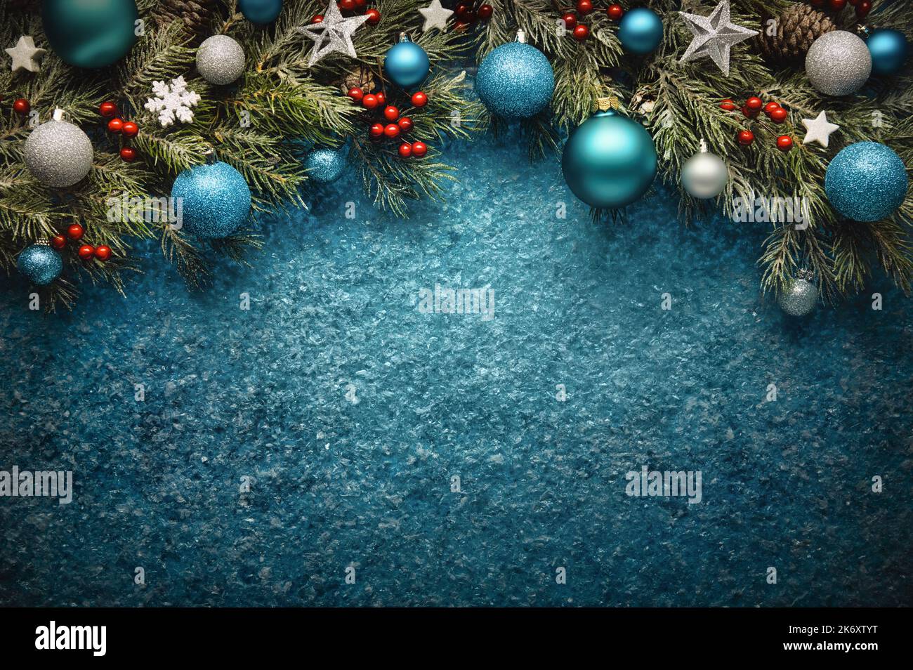 Christmas background in turquoise blue, with textured copy-space and an arch-shaped border composed of fir branches, baubles, stars and holly Stock Photo