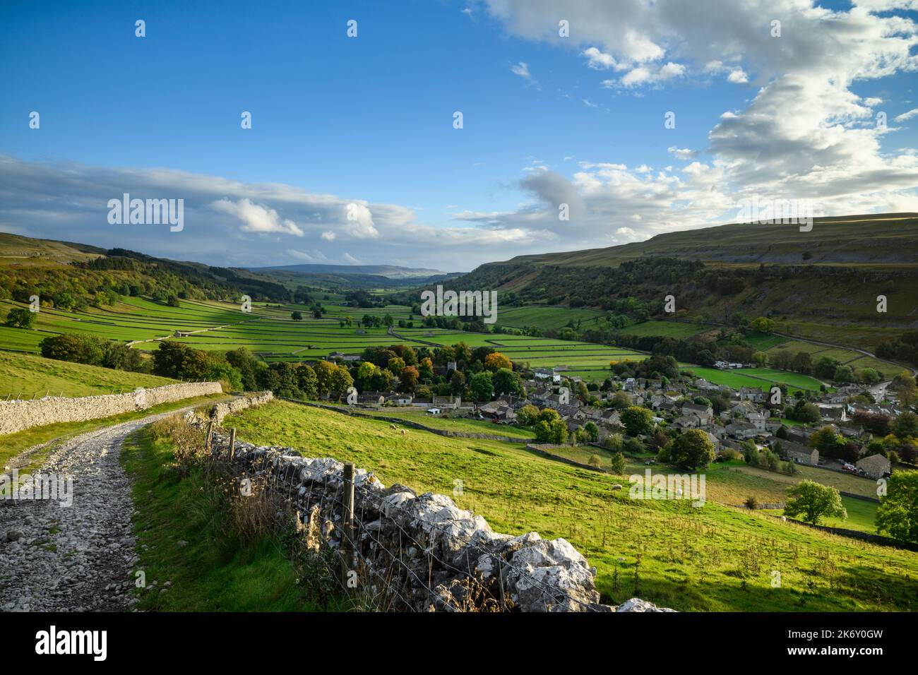 Picturesque Dales view (wide sunlit u-shaped valley, steep hillside slopes, cottages & houses, dramatic blue sky) - Kettlewell, Yorkshire, England UK. Stock Photo