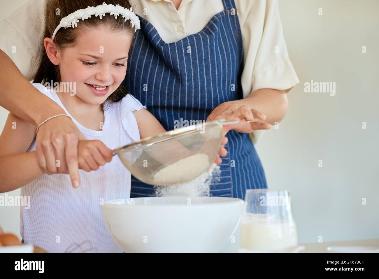 She knows the best techniques. a little girl helping her parent cook in the kitchen at home. Stock Photo