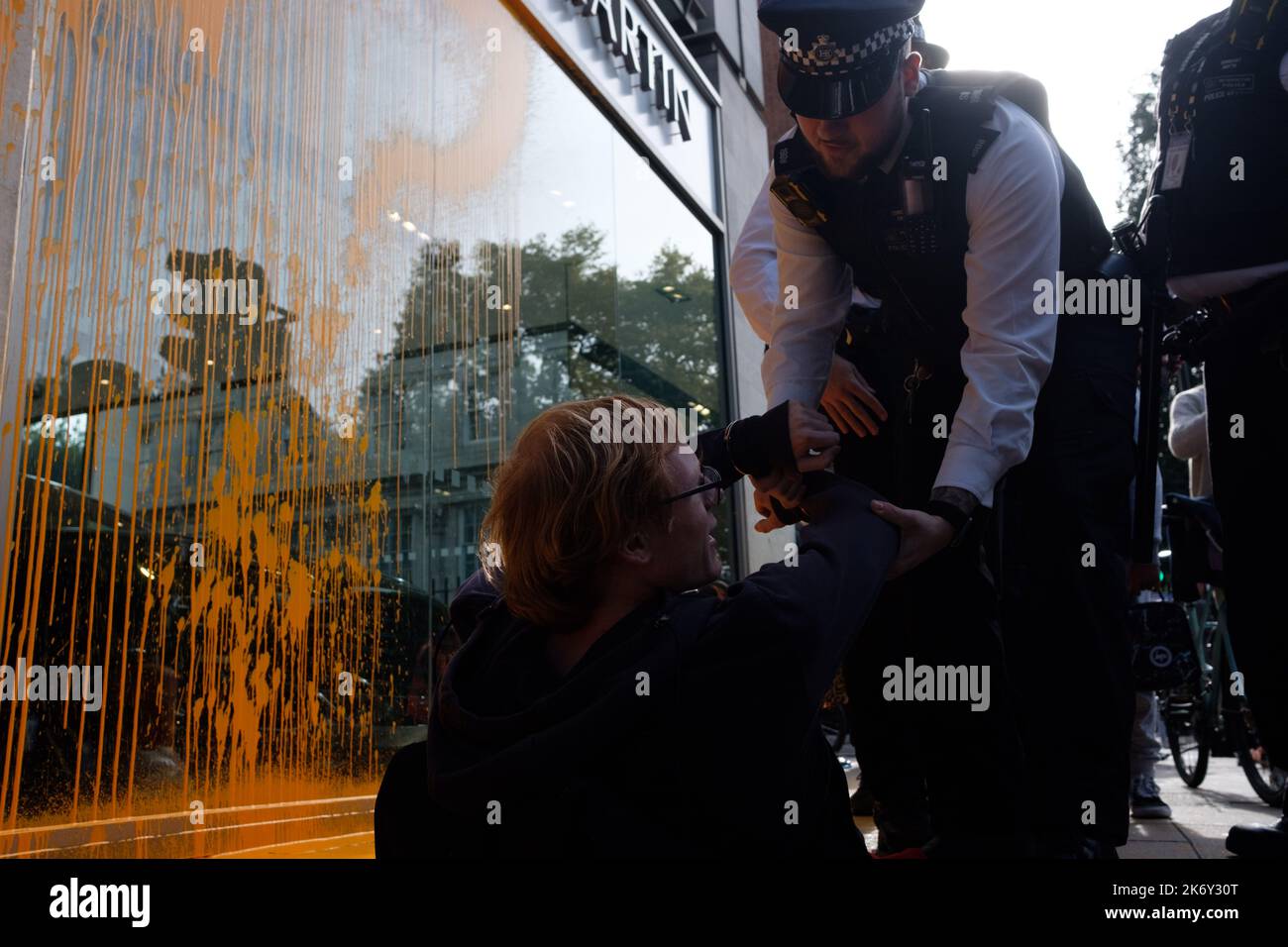 London, UK. 16 OCT, 2022. Just Stop Oil activists covered the Aston Martin showroom in Park Lane with orange paint and blocked the road. Members of the public drag an activists who are blocking the road. Police officers detain an activist after paint was thrown over a car showroom window. Credit: Joao Daniel Pereira/Alamy Live News Stock Photo