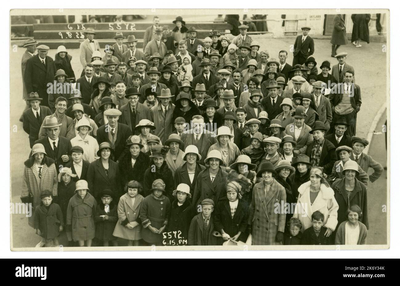 Original 1920's era postcard of large crowd at the seaside, photographed by the pier. published by B.B. Photo series dated 9 August 1925 6.16pm, printed on front. Some characters, lots of fashions, including  lady's cloche hats and men's homburg hats and flat caps. Bournemouth, England, UK. Stock Photo