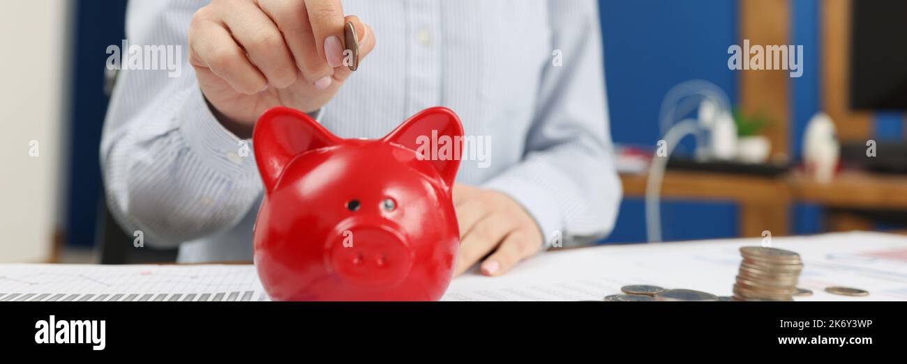 A woman puts a coin in a red piggy bank Stock Photo - Alamy