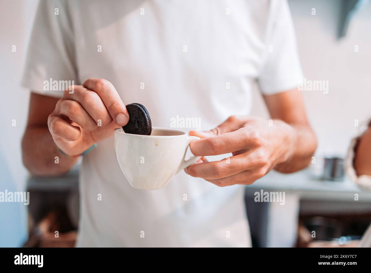 Male hand dipping a black sandwich biscuit into milk Stock Photo