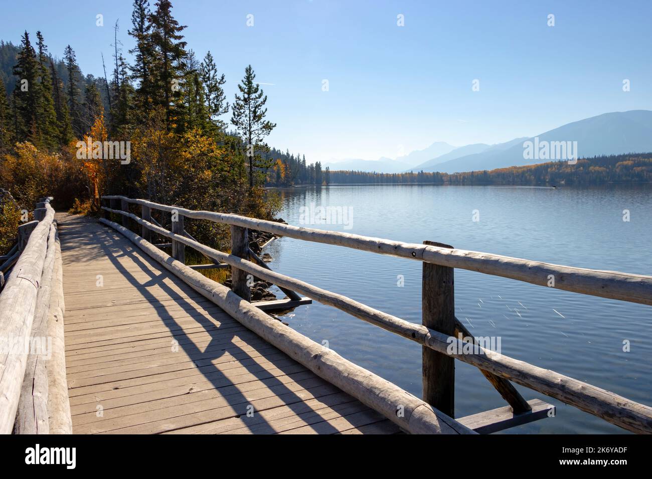 autumn scene of walkway across lake leading to trees with faint mountains in background Stock Photo