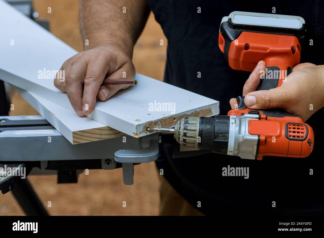 Using screwdriver, he drills holes in wooden boards in order to connect