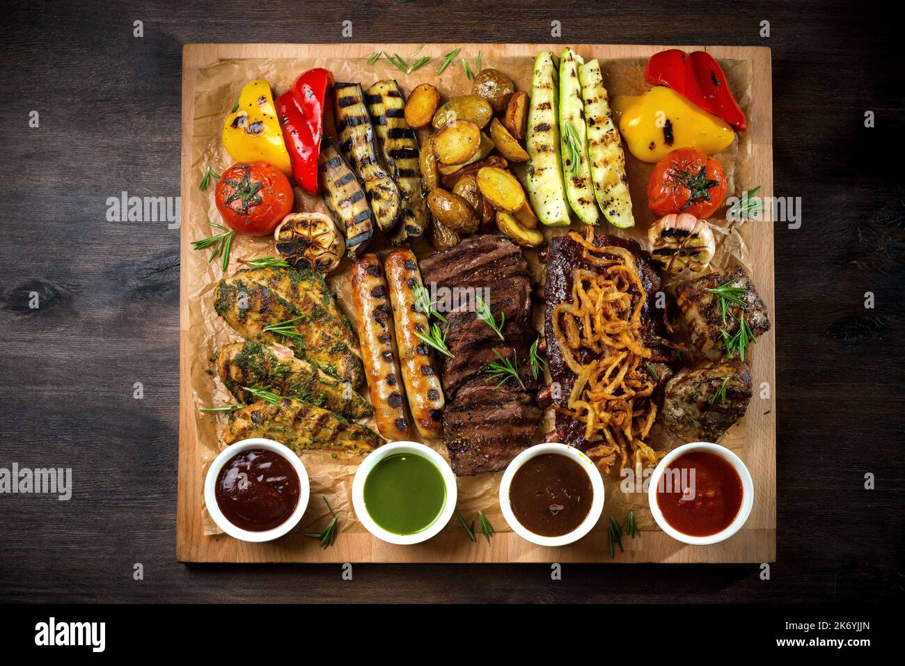 A board with grilled appetizers and sauces. Grilled vegetables and meat snacks: sausages, chicken fillets, pork and beef steaks. Stock Photo