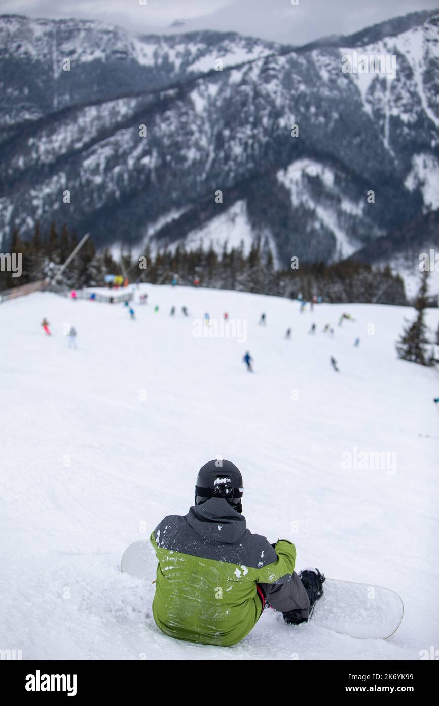 man snowboarder sitting on the slope enjoying the view Stock Photo